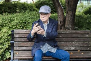 公園でスマホを見るシニア男性（遠距離介護のイメージ）