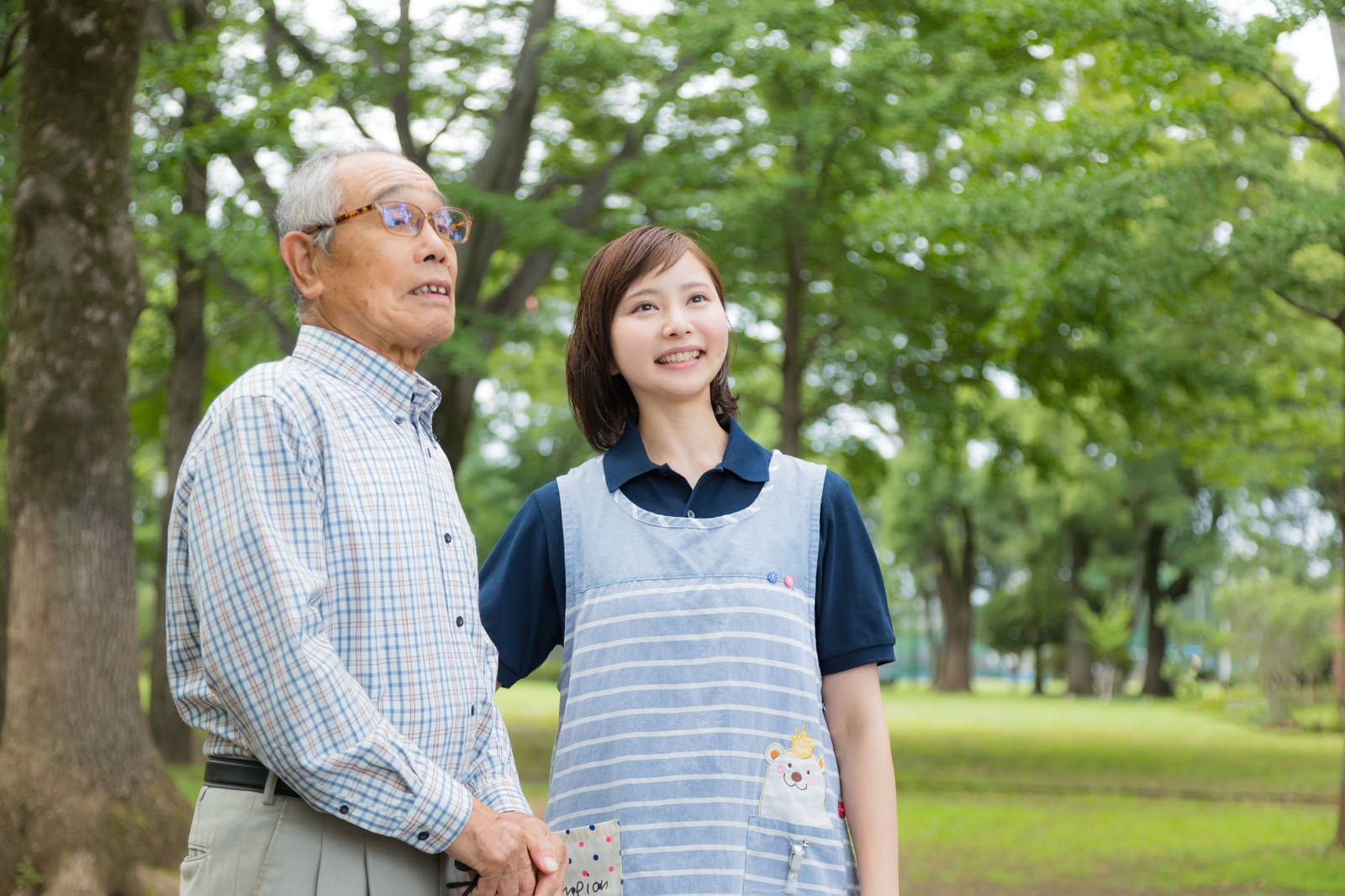 公園を散歩する高齢者と付添い（認知症の徘徊・見守りのイメージ）